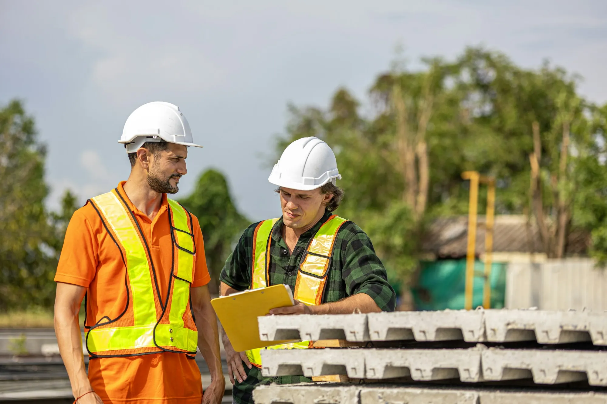 Two electricians in hard hats reviewing a job plan on a clipboard