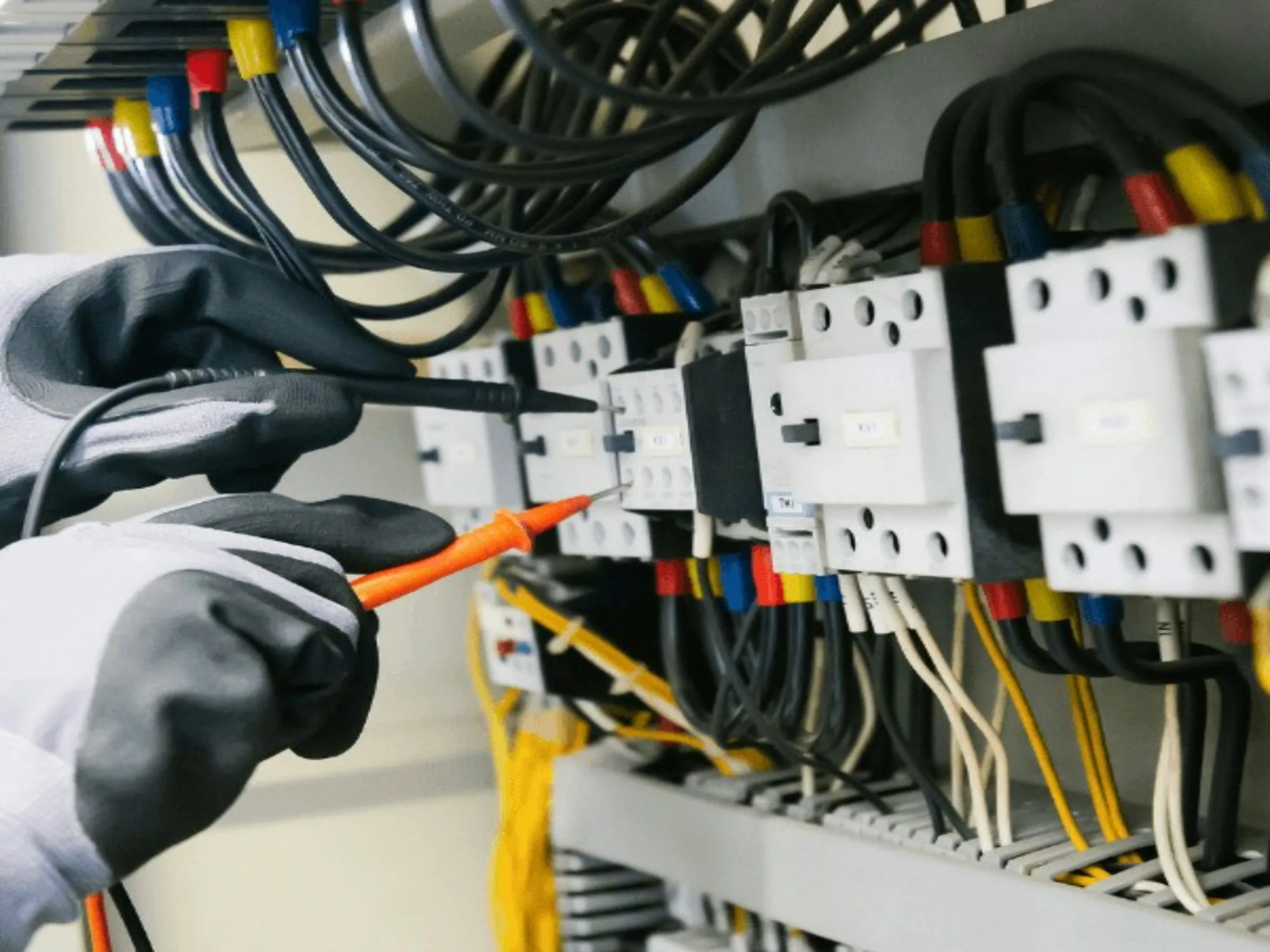 Gloved hand testing a breaker row in an electrical panel with a probe