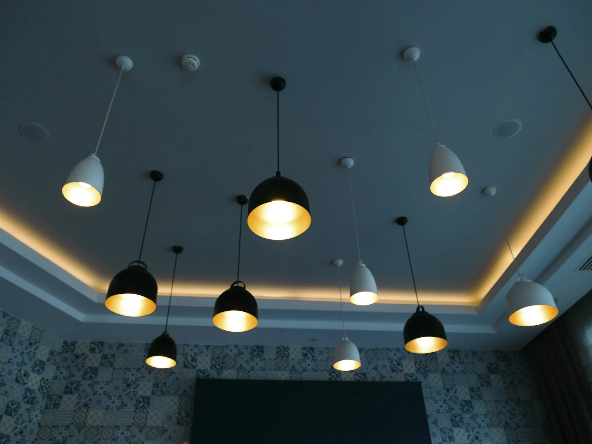 Row of pendant lights hanging from a dark ceiling with recessed lighting