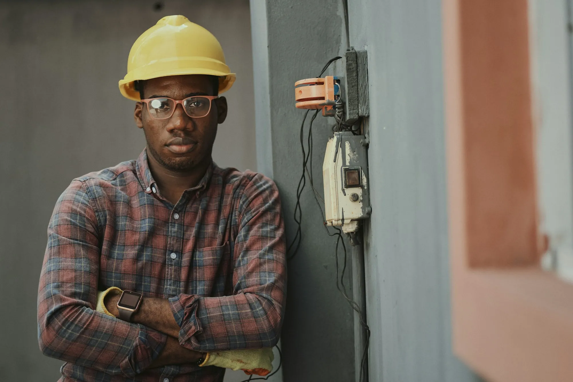 Electrician standing beside a wall-mounted electrical meter and panel