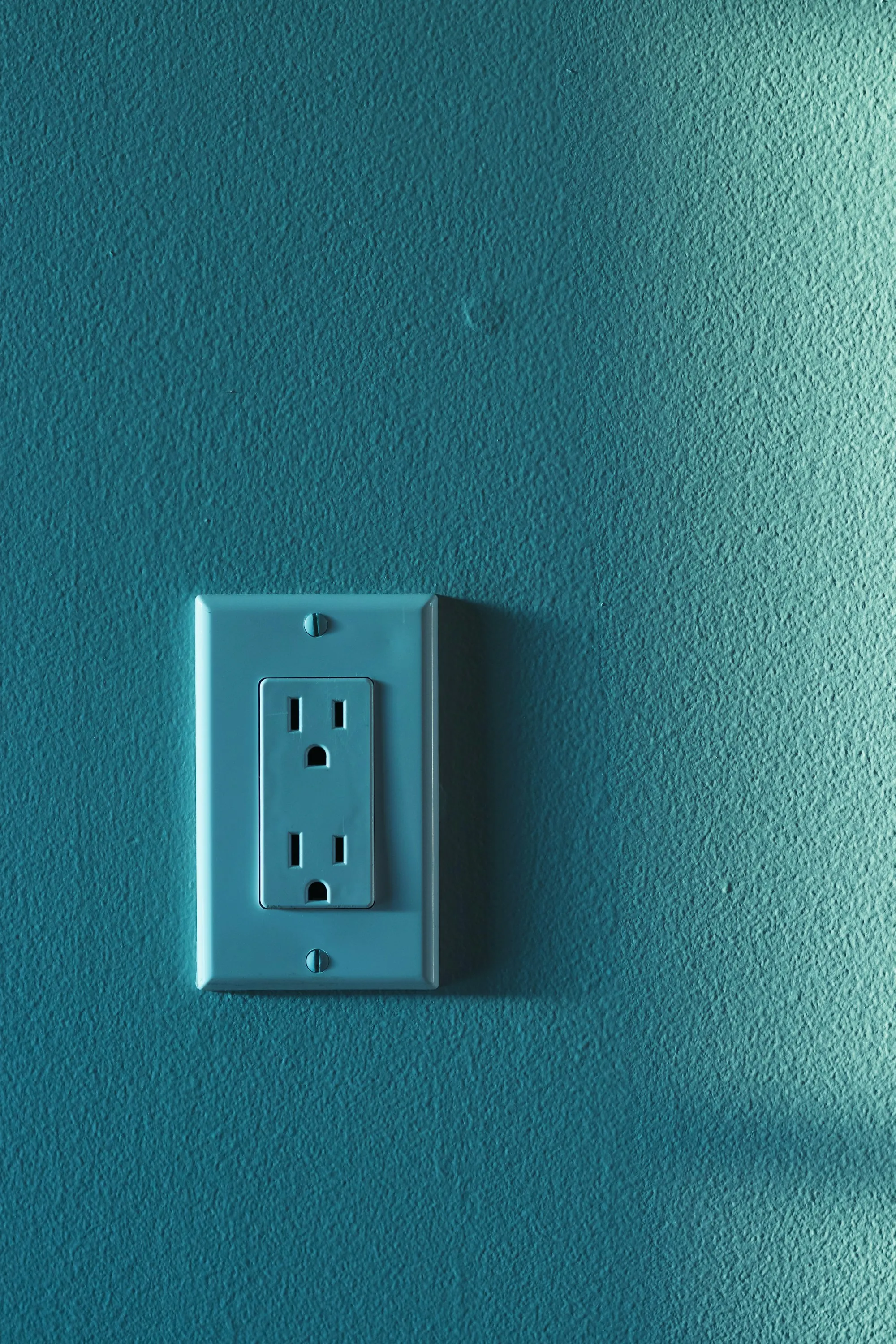 Single white electrical outlet on a teal painted wall